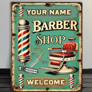 Op de afbeelding: Vintage-stijl kapperssalon bord met rood-wit-blauwe gestreepte kapperssalon palen, een rode leren kappersstoel en de tekst "YOUR NAME BARBER SHOP WELCOME".