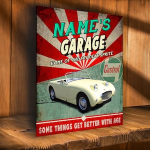 May include: A vintage-style garage sign with red, white, and green colors. The sign features a white classic car with a red and white striped background. The text on the sign reads "NAME'S GARAGE, HOME OF THE FROGEYE SPRITE, SOME THINGS GET BETTER WITH AGE".