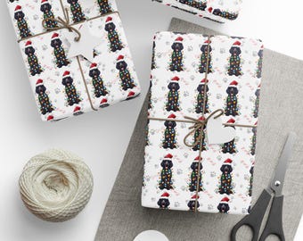 Puede incluir: Papel de regalo blanco con un patrón repetitivo de perros negros con gorros de Papá Noel rojos y envueltos en luces navideñas de colores, acentuado con pequeñas huellas grises y formas de huesos rosas, atado con cuerda marrón y etiquetas.