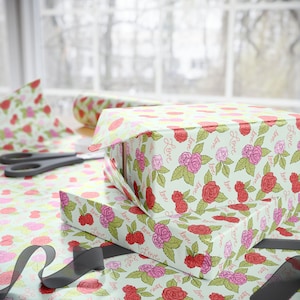 May include: Gift boxes wrapped in floral paper with red and pink roses and the word "Love" printed on a light green background. Scissors and a roll of wrapping paper are also visible.