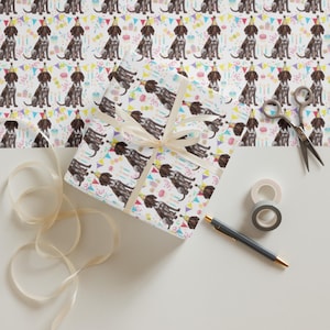 May include: White wrapping paper with a repeating pattern of brown and white dogs wearing party hats and holding birthday cake. The dogs are surrounded by colorful confetti and flags.