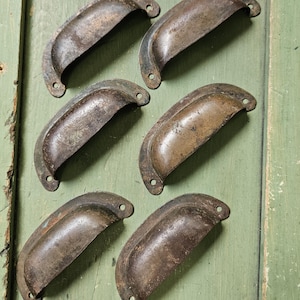 May include: A set of six semi-circular metal drawer pulls with a dark, weathered, and oxidized finish. Each handle features a curved grip and two small circular mounting holes at the ends, displaying a consistent aged patina across all pieces.
