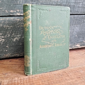 May include: A vintage green book titled "Orton's Lightning Calculator and Accountant's Assistant" with gold lettering. The book is standing upright on a wooden surface, with a weathered green wooden background.