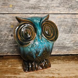 May include: A ceramic owl figurine with brown and teal glaze. The owl has large, round eyes with concentric circles in the glaze.