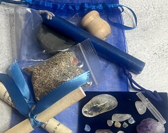 May include: A collection of spiritual items, including a blue candle, small crystals, a wooden item, and a bag of herbs. The items are arranged on a light gray surface, with a blue drawstring bag and blue ribbons.