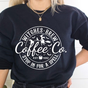 May include: Black sweatshirt with a white circular graphic that reads "Witches Brew Coffee Co." with a witch on a broom, bats, and the text "Stop in for a spell." The sweatshirt is a crew neck style.