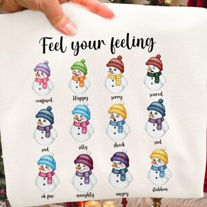 May include: White fabric with the text "Feel your feeling" and illustrations of snowmen expressing different emotions. Each snowman wears a hat, scarf, and has a corresponding emotion label, such as "confused" or "happy."