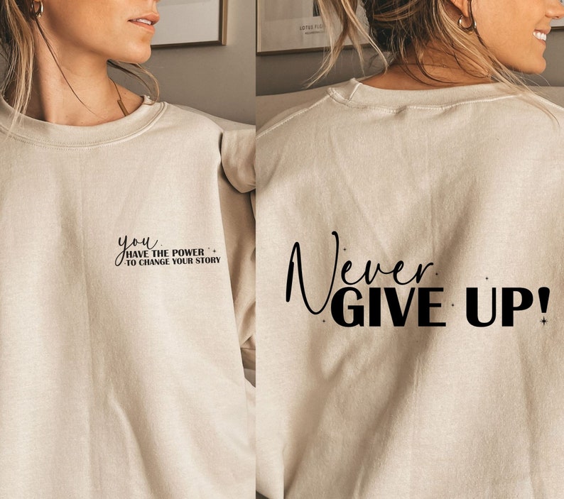 Op de afbeelding: Een beige sweatshirt met de tekst "you have the power to change your story" op de voorkant en "Never Give Up!" op de achterkant.