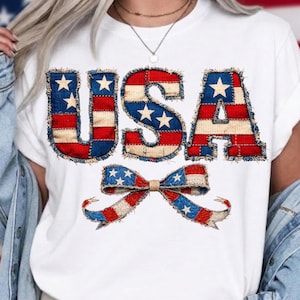 Puede incluir: Camiseta blanca con la palabra "USA" en un diseño de patchwork con colores rojo, blanco y azul, y estrellas. Un lazo a juego está debajo del texto, también en rojo, blanco y azul.