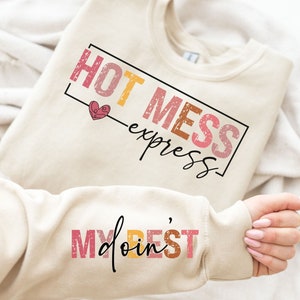May include: A cream colored sweatshirt with the text "HOT MESS express" in a colorful, distressed font. The sweatshirt also has the text "My doin' BEST" on the sleeve in a similar font.