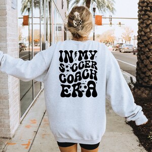 May include: A gray sweatshirt with a black graphic that says "In My Soccer Coach Era" with a lightning bolt and soccer ball.