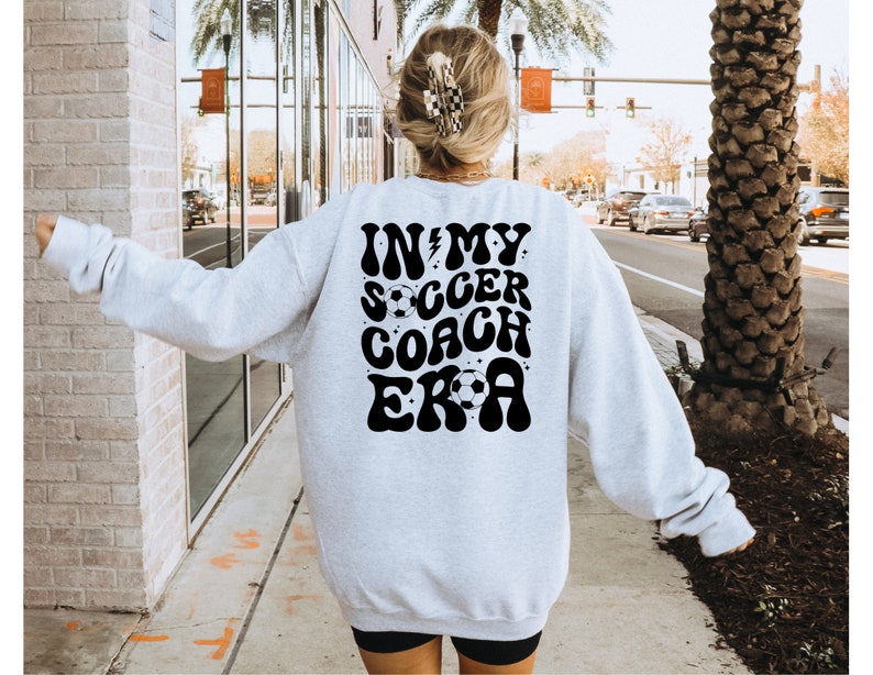 May include: A gray sweatshirt with a black graphic that says "In My Soccer Coach Era" with a lightning bolt and soccer ball.