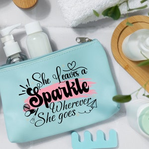 May include: A light blue zippered makeup bag with a pink and white design. The bag has the text "She leaves a sparkle wherever she goes" printed on it.
