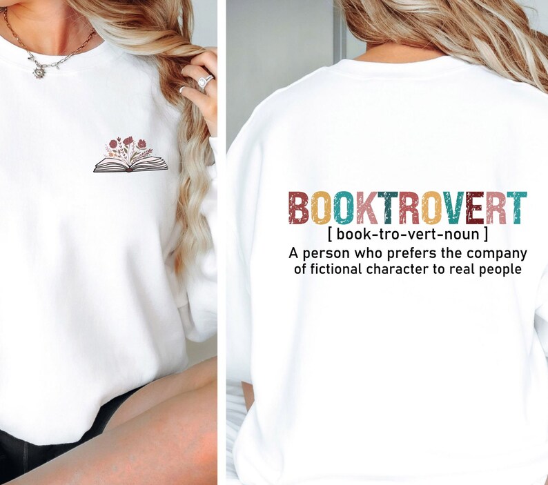 K&ouml;nnte beinhalten: Wei&szlig;er Pullover mit einem Buch- und Blumenmotiv auf der Vorderseite und dem Text "BOOKTROVERT [book-tro-vert-noun] A person who prefers the company of fictional character to real people" auf der R&uuml;ckseite.