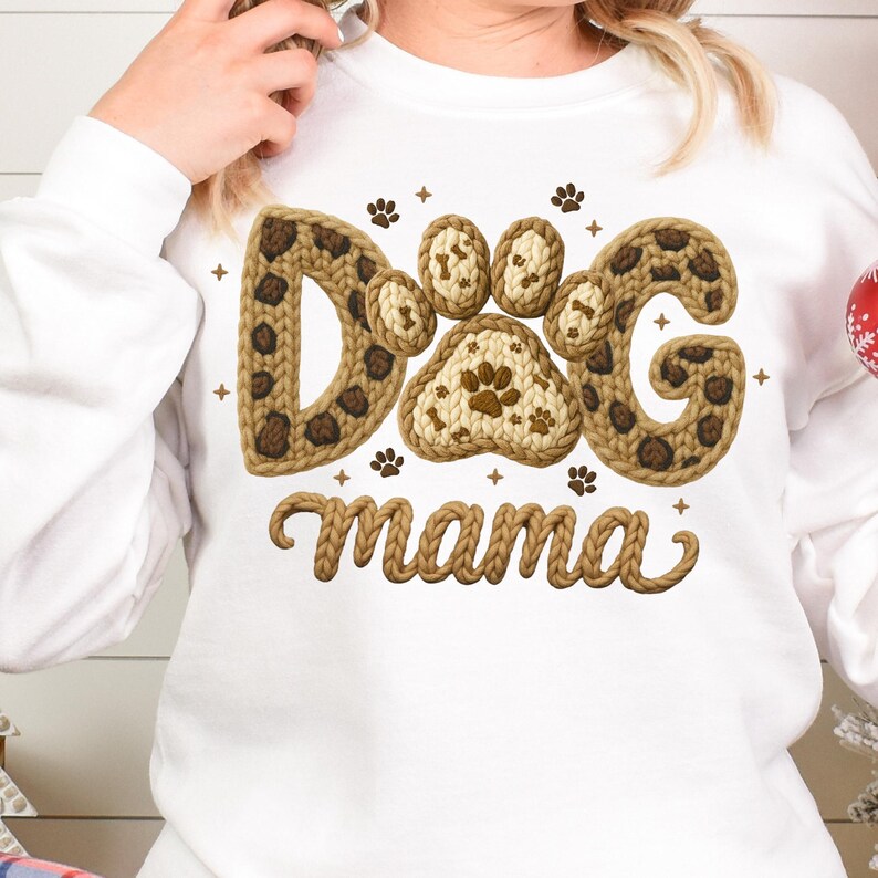 May include: White sweatshirt with a brown and tan "Dog Mama" design. The design features the words "Dog Mama" in a knitted style, with paw prints and a leopard print pattern.