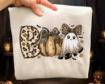 Może przedstawiać: Kremowa bluza z motywem Halloween z napisem "BOO" w wzór w cętki. "O" to dynia z kokardą w cętki, a drugie "O" to duch z kokardą w cętki. Nietoperze i liście są rozrzucone wokół wzoru.
