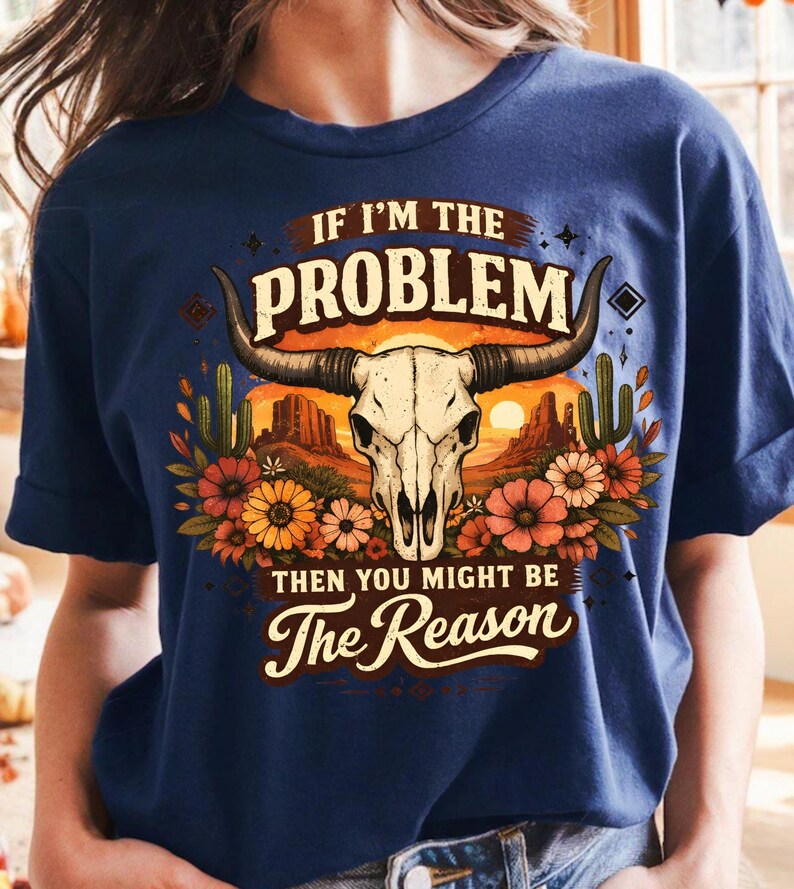 May include: Navy blue t-shirt featuring a graphic of a bull skull with horns, surrounded by flowers, cacti, and a desert landscape. The text reads "IF I'M THE PROBLEM THEN YOU MIGHT BE The Reason."