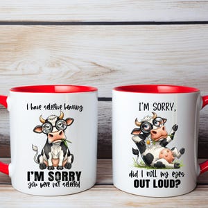 May include: Two white ceramic mugs with red interiors and handles. Each mug features a cartoon cow wearing glasses. One mug reads "I have selective hearing" and "I'm sorry you were not selected." The other mug reads "I'm sorry, did I roll my eyes out loud?"