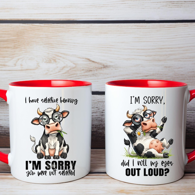 May include: Two white ceramic mugs with red interiors and handles. Each mug features a cartoon cow wearing glasses. One mug reads "I have selective hearing" and "I'm sorry you were not selected." The other mug reads "I'm sorry, did I roll my eyes out loud?"