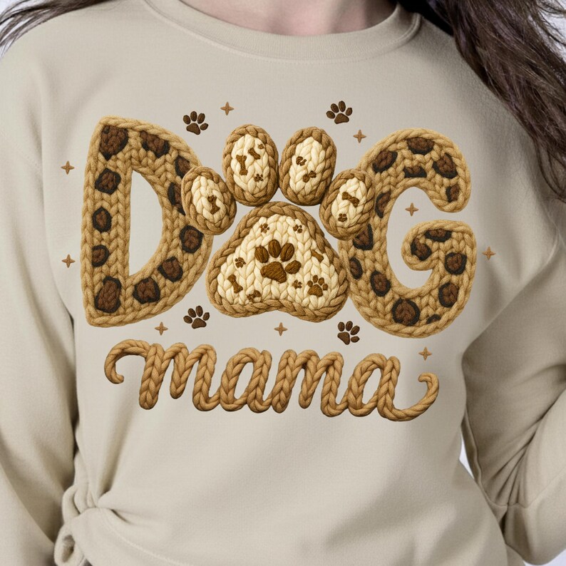 May include: A beige sweatshirt featuring the words "Dog Mama" in a decorative font. The word "Dog" is designed with a paw print and bone pattern. The sweatshirt is a comfortable and casual style.