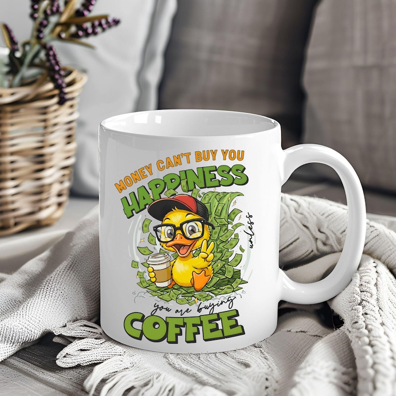 May include: White ceramic coffee mug with a cartoon duck wearing glasses and a cap, holding a coffee cup. The mug features the text "Money can't buy you happiness unless you are buying coffee."