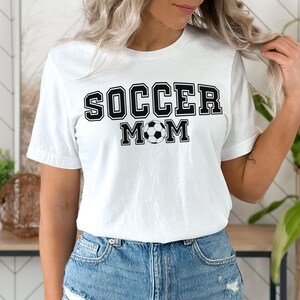 Puede incluir: Camiseta blanca con texto negro que dice "Soccer Mom" y un gr&aacute;fico de bal&oacute;n de f&uacute;tbol blanco y negro.