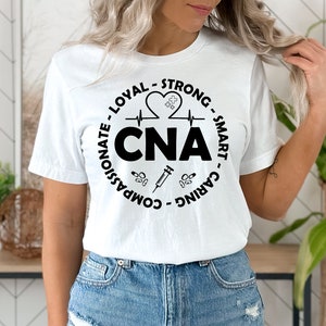 May include: White t-shirt with a black circle graphic that says "CNA" and includes a heart with a heartbeat line, a syringe, and pills. The text around the circle says "Caring - Smart - Strong - Loyal - Compassionate".