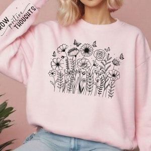 Może przedstawiać: R&oacute;żowa bluza z czarnym rysunkiem kwiat&oacute;w i motyli. Na rękawie znajduje się napis "GROW positive THOUGHTS".