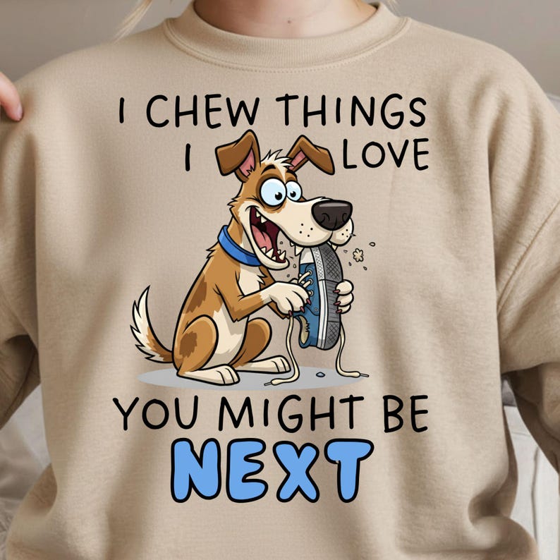 May include: Beige sweatshirt with a cartoon dog chewing a blue and gray shoe. The text reads "I CHEW THINGS I LOVE YOU MIGHT BE NEXT" in black and blue block letters. The dog is brown and white with a blue collar.