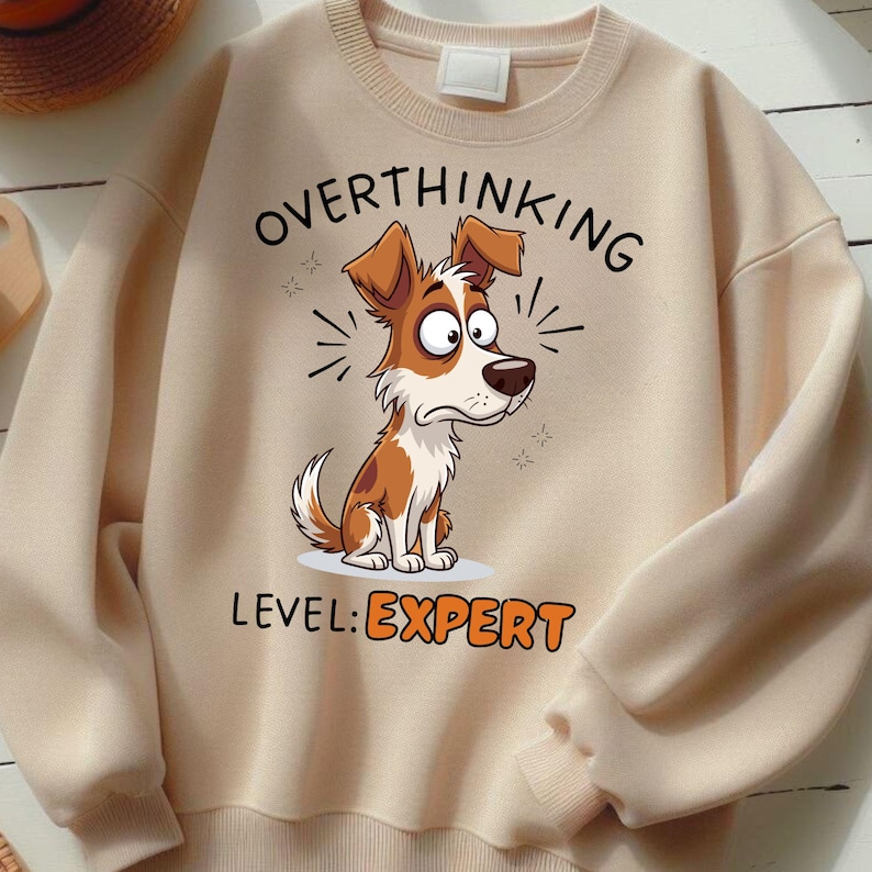May include: Beige sweatshirt with the words "OVERTHINKING" above a cartoon dog illustration. The dog is brown and white with a worried expression. Below the dog, the text reads "LEVEL: EXPERT".