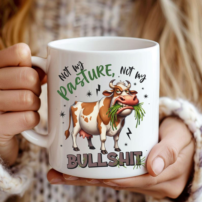 May include: White ceramic mug featuring a cartoon cow with brown and white spots, eating grass. The mug has the text "Not my pasture, not my bullshit" in green and gray. Lightning bolt and star graphics are also present.