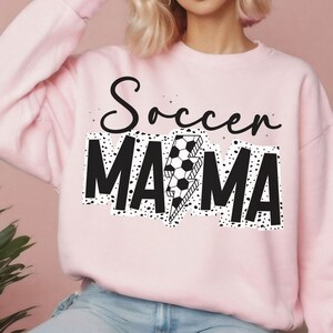 Puede incluir: Sudadera rosa con texto negro que dice "Soccer Mama" con un rayo y un bal&oacute;n de f&uacute;tbol.