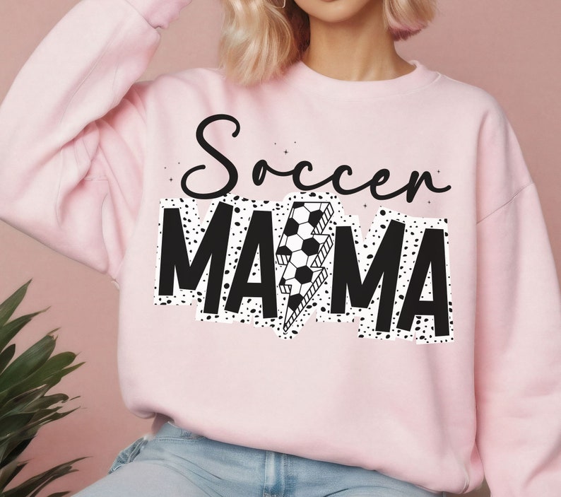 Puede incluir: Sudadera rosa con texto negro que dice "Soccer Mama" con un rayo y un bal&oacute;n de f&uacute;tbol.