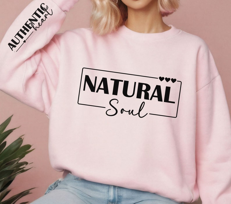 Może przedstawiać: R&oacute;żowa bluza z napisem "NATURAL Soul" w czarnym prostokącie z małymi sercami nad tekstem. Lewy rękaw ma napis "AUTHENTIC heart" w kolorze czarnym.