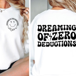 May include: White sweatshirt with a black graphic on the front that says "Dreaming of Zero Deductions" with a smiley face and lightning bolts for eyes. The back of the sweatshirt has the same text in a larger font.