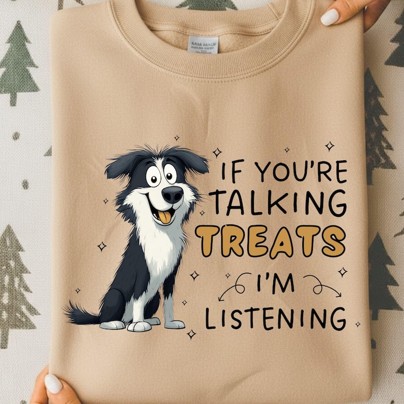 May include: A tan sweatshirt featuring a cartoon dog with black and white fur. The dog has a happy expression and the text "IF YOU'RE TALKING TREATS I'M LISTENING" is printed on the front.