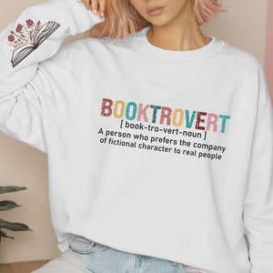 K&ouml;nnte beinhalten: Wei&szlig;er Pullover mit dem Text "BOOKTROVERT [book-tro-vert-noun] A person who prefers the company of fictional character to real people" in bunten Buchstaben.