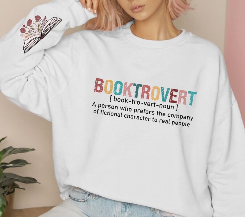 K&ouml;nnte beinhalten: Wei&szlig;er Pullover mit dem Text "BOOKTROVERT [book-tro-vert-noun] A person who prefers the company of fictional character to real people" in bunten Buchstaben.