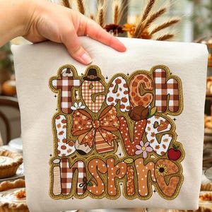 May include: Cream-colored sweatshirt with the words "Teach Love Inspire" in a fall-themed design. The design includes pumpkins, a bow, and a turkey, with a mix of plaid and floral patterns.