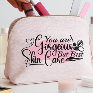 May include: Pink cosmetic bag with a white and pink brushstroke design and the text "You are gorgeous but first skin care".
