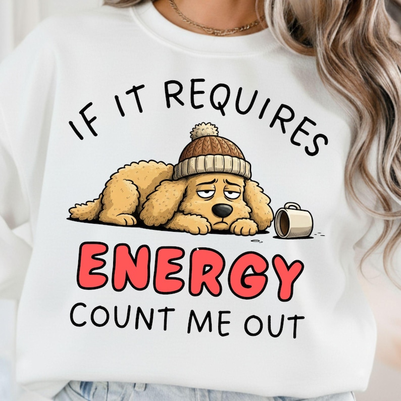 May include: White sweatshirt with a cartoon illustration of a tired-looking dog wearing a knit cap. The text reads "If it requires energy, count me out" in black and red lettering. A coffee mug is next to the dog.