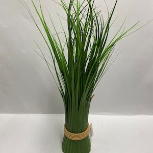 May include: A bunch of artificial green grass tied with a natural rope. The grass blades are long and slender, with a slight curve. The base is a darker green, and the rope adds a rustic touch. A small tag is attached.