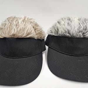 Peut inclure: Deux casquettes noires avec visière et des cheveux factices sur le dessus. L'une a des cheveux brun clair et l'autre des cheveux gris.