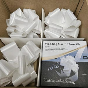 May include: A white wedding car ribbon kit in a cardboard box. The kit includes 9 meters of waterproof ribbon and 3 matching assembled pull bows. The box also contains several large, pre-made white bows.