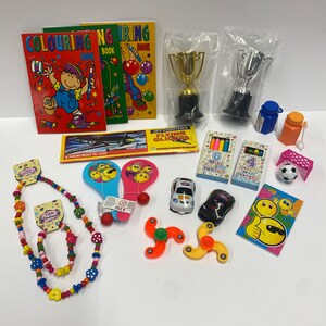 May include: A collection of party favour items including colouring books, toy cars, a football, a necklace, a pair of paddle ball bats, a spinning top, crayons, pencils, and two gold and silver trophy cups.