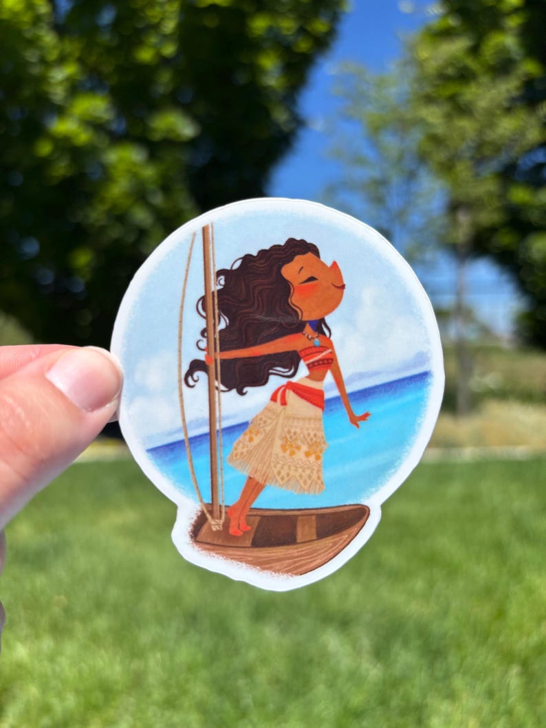May include: A circular sticker featuring a cartoon illustration of a person with long dark wavy hair, wearing a red and beige patterned outfit, standing on a small wooden boat with a mast, set against a bright blue ocean and sky background.