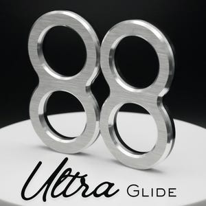 May include: Two brushed metal number eight shapes, side by side, on a white surface. The shapes have a circular design with a brushed metal finish. The word "Ultra" is written in cursive, and the word "GLIDE" is written in a sans-serif font.