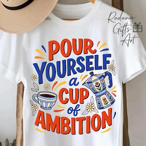 May include: A white short-sleeved t-shirt featuring a graphic with the text "POUR YOURSELF a CUP of AMBITION" in orange and blue. The design includes a blue coffee cup, a blue moka pot with floral details, and small white daisy flowers.