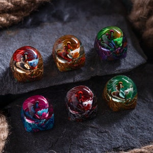 Può includere: Sei keycap in resina con scene in miniatura colorate e dettagliate all'interno. Ogni keycap presenta una scena diversa con una base dorata.