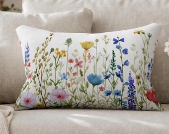 Könnte beinhalten: Ein rechteckiges Zierkissen mit weißem Hintergrund und einem farbenfrohen Aquarelldruck verschiedener Wildblumen, darunter blaue, gelbe, rosa und rote Blüten mit grünen Stängeln und Blättern, die auf der Vorderseite angeordnet sind.